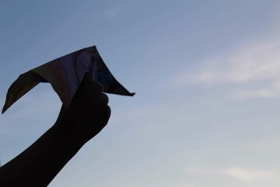 Low angle view of hand holding flag against sky