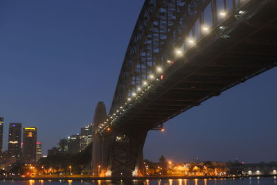 Low angle view of illuminated bridge against buildings at night
