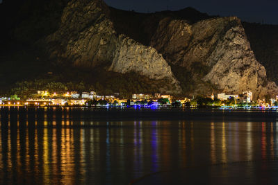 Illuminated built structure by river against sky at night