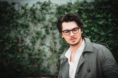 Man wearing eyeglasses standing against plants