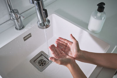 From above top view cropped unrecognizable child boy washing hands under running water carefully in modern bathroom at home