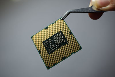 Close-up of hand holding computer chip against gray background