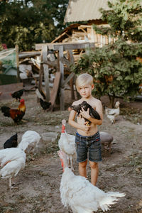 Shirtless boy holding hen standing at poultry