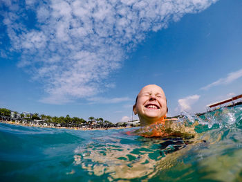 Smiling girl swimming in sea against sky