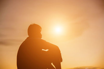 Rear view of silhouette man standing against orange sky