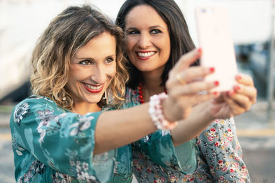 Cheerful female friends taking selfie while standing outdoors