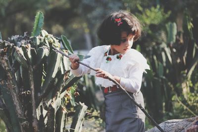 Girl holding stick while standing by plant