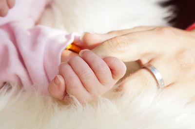 Cropped image of baby and parent holding hands on rug