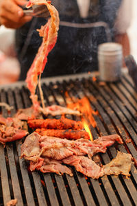 Cropped hand of person preparing meat on barbecue grill