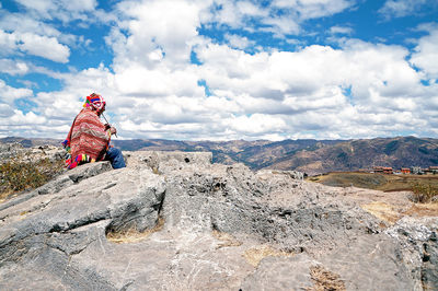 Man playing flute while sitting on rock against sky