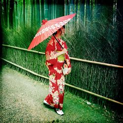 Woman with paper umbrella walking by fence