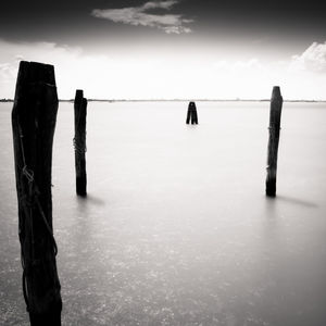 Wooden posts in sea against sky