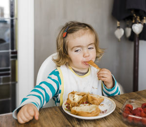 Cute girl eating food on table at home