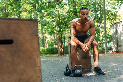 Full length of shirtless young man sitting in city