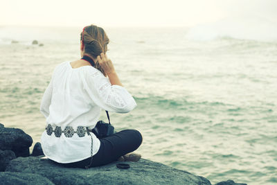 Rear view of woman sitting on rock at beach