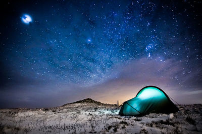 Illuminated tent on snow covered field at night