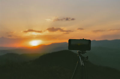 Tilt image of camera against sky during sunset