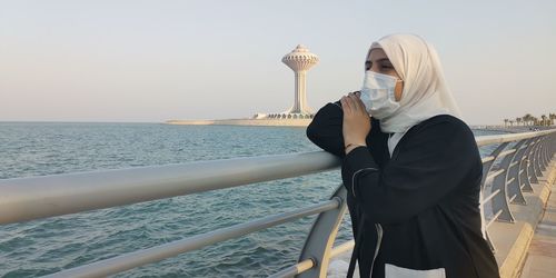 Woman standing on railing by sea against sky