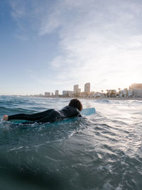 Side view of young female surfer in wetsuit lying on waving seawater and enjoying summer day