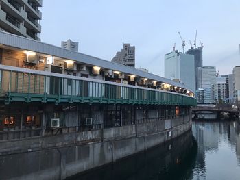 Illuminated bridge over river by buildings against sky in city