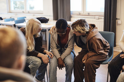 Female friends consoling sad teenage girl in group therapy