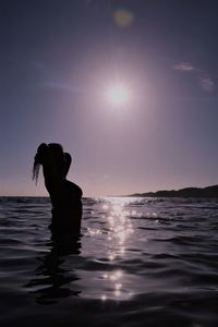 Silhouette woman in sea against sky during sunset