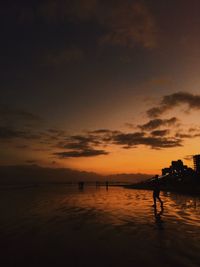 Silhouette man standing on shore at beach against sky during sunset