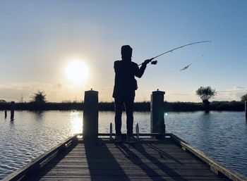 Silhouette man fishing at lake against sky during sunset