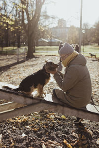 Side view of man bonding with dog while sitting at park during autumn