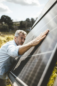Mature man touching solar panels in garden on sunny day