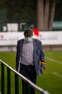 Man walking away from the soccer field in the rain wearing a mouth mask