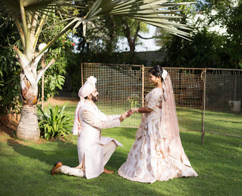 Groom putting ring in bride finger on lawn