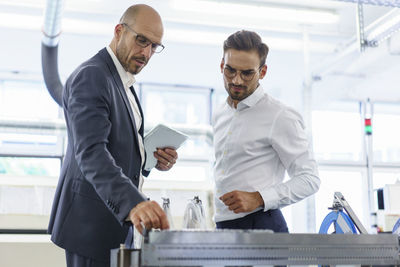 Confident male professionals discussing over machinery against machinery at factory