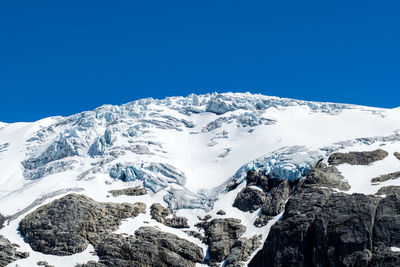 Low angle view of snowcapped mountains against clear blue sky