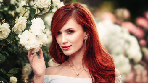 Portrait of beautiful woman holding flower while standing outdoors
