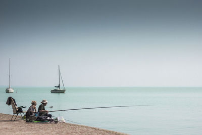 People sitting sear seashore for fishing against clear sky