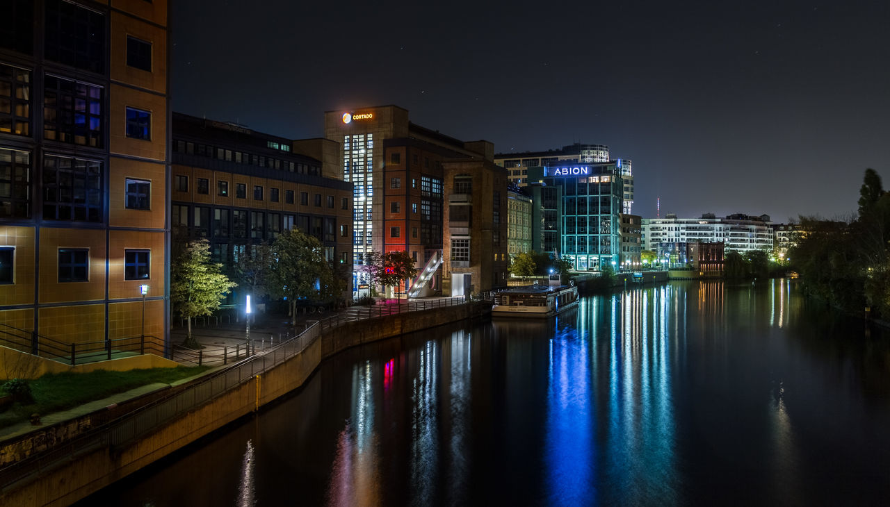 ILLUMINATED BUILDINGS BY RIVER AT NIGHT