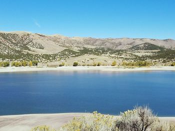 Scenic view of lake and mountains against clear blue sky