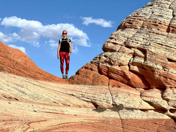 Front view of woman standing on colorful desert  rock formations against blue sky and clouds
