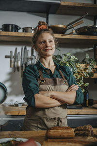 Confident female chef looking away while standing with arms crossed in kitchen
