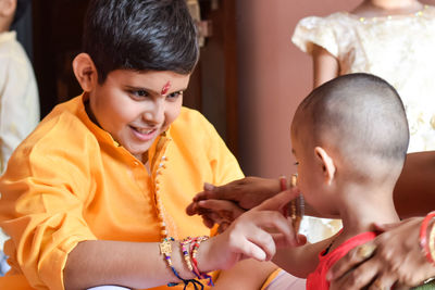 Boy wearing rakhis while sitting with toddler sister at home