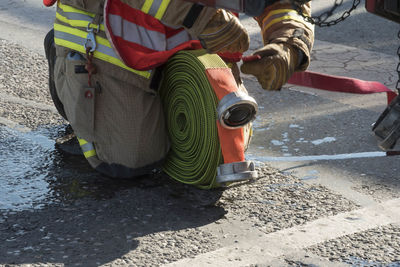 Low section of firefighter holding fire hose on road