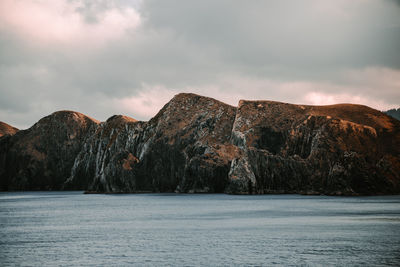 Scenic view of sea by mountain against sky