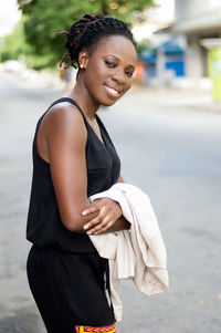 Smiling young woman standing by the roadside looks to her left before crossing the track.