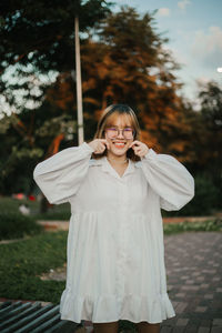 Portrait of young woman with arms outstretched standing against trees