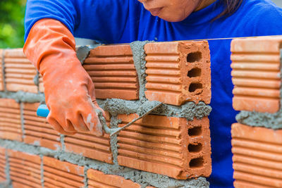 Construction worker laying down brick wall using mortar to join and fill in the gap between bricks