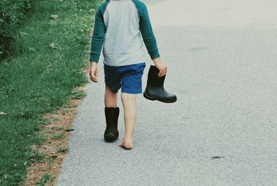 Rear view of boy holding rubber boot while walking on road