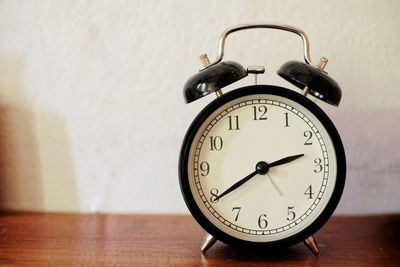 Close-up of alarm clock on table against wall