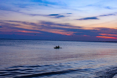 Distant rowboat on calm sea at sunset