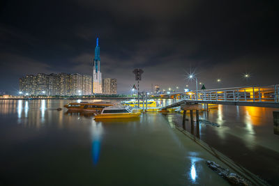 Illuminated bridge over river by buildings against sky at night